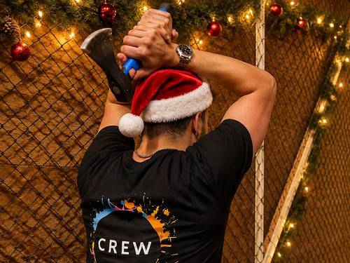 Crew-Mitglied mit Weihnachtsmütze holt zum Axtwurf aus
